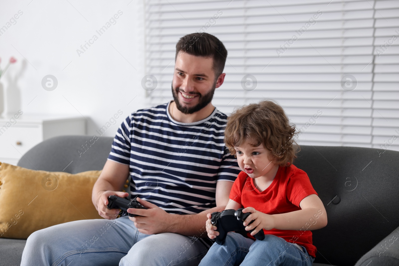 Happy father and his son playing with game controllers together on sofa at home Photo of Happy father and his son playing with game controllers together on sofa at home