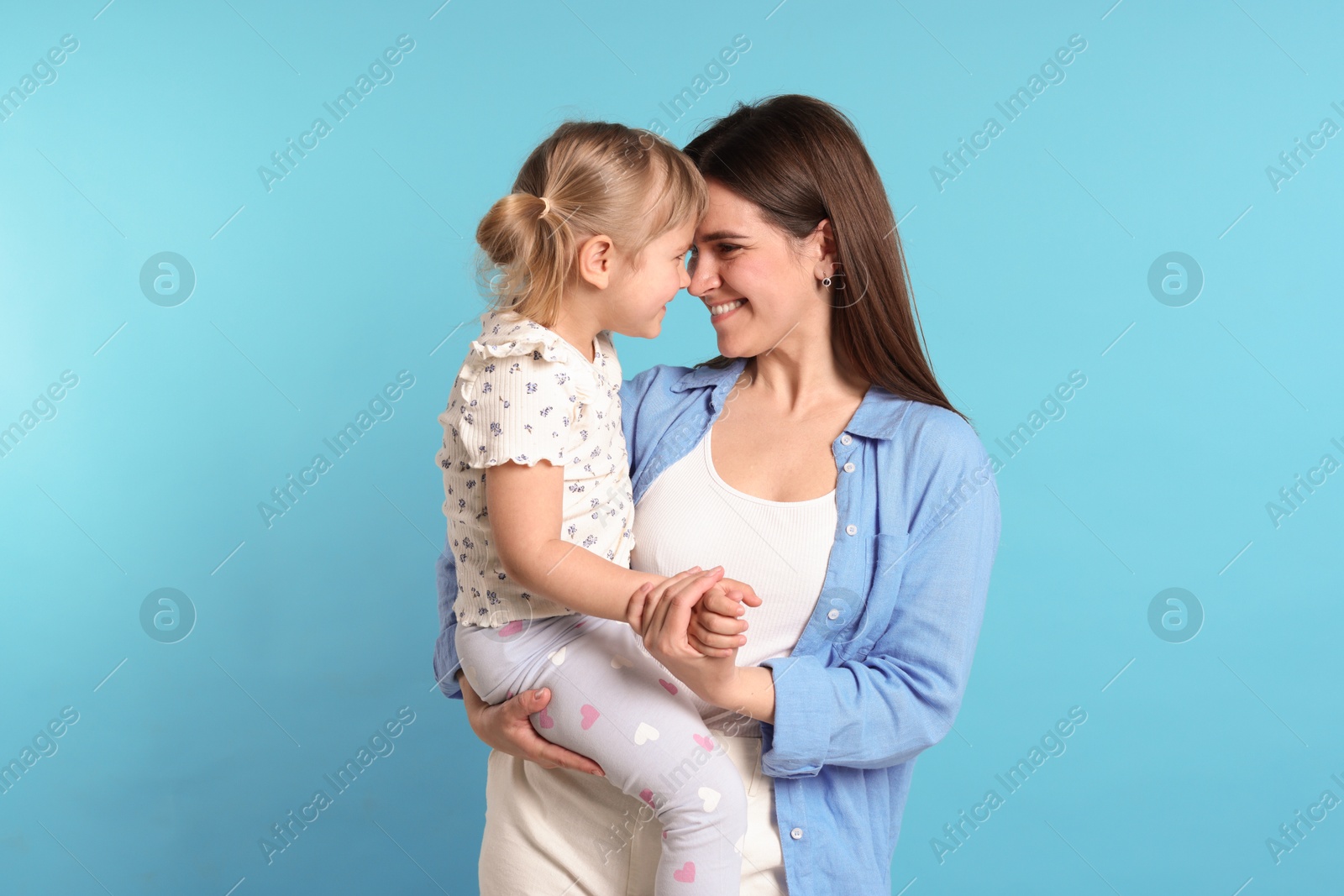 Happy mother and her cute daughter on light blue background Photo of Happy mother and her cute daughter on light blue background