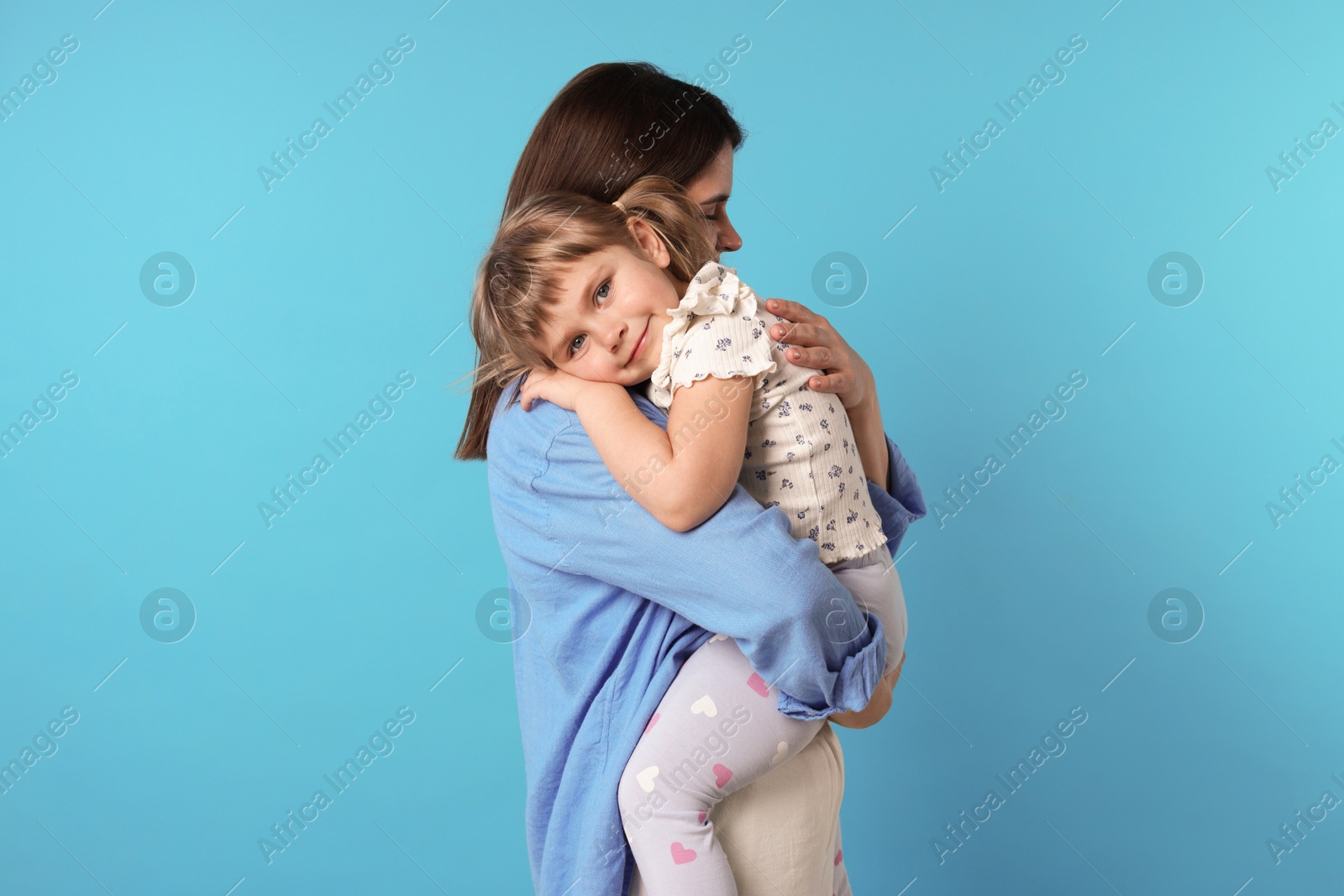 Happy mother and her cute daughter on light blue background Photo of Happy mother and her cute daughter on light blue background