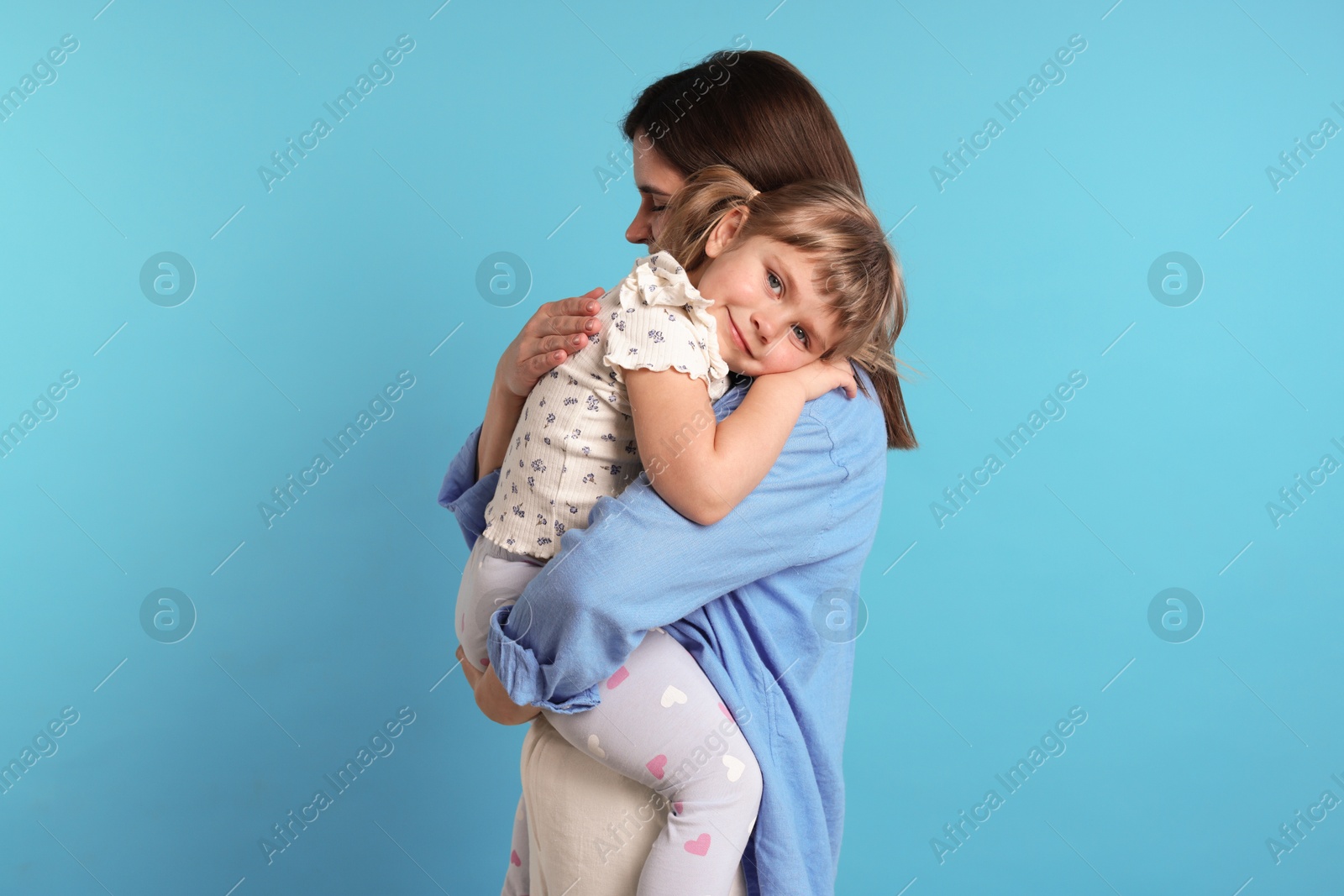 Happy mother and her cute daughter on light blue background Photo of Happy mother and her cute daughter on light blue background