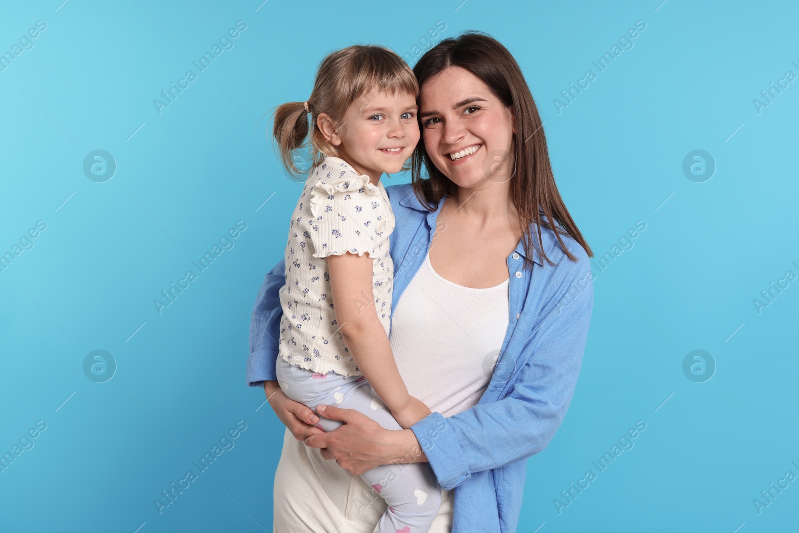 Happy mother and her cute daughter on light blue background Photo of Happy mother and her cute daughter on light blue background