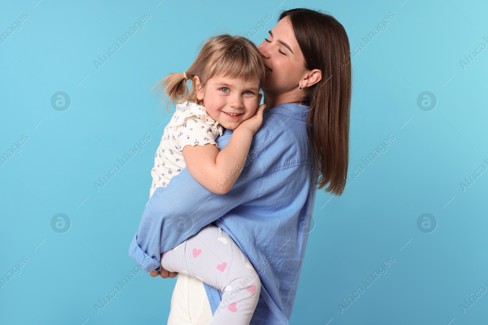 Happy mother and her cute daughter on light blue background Photo of Happy mother and her cute daughter on light blue background