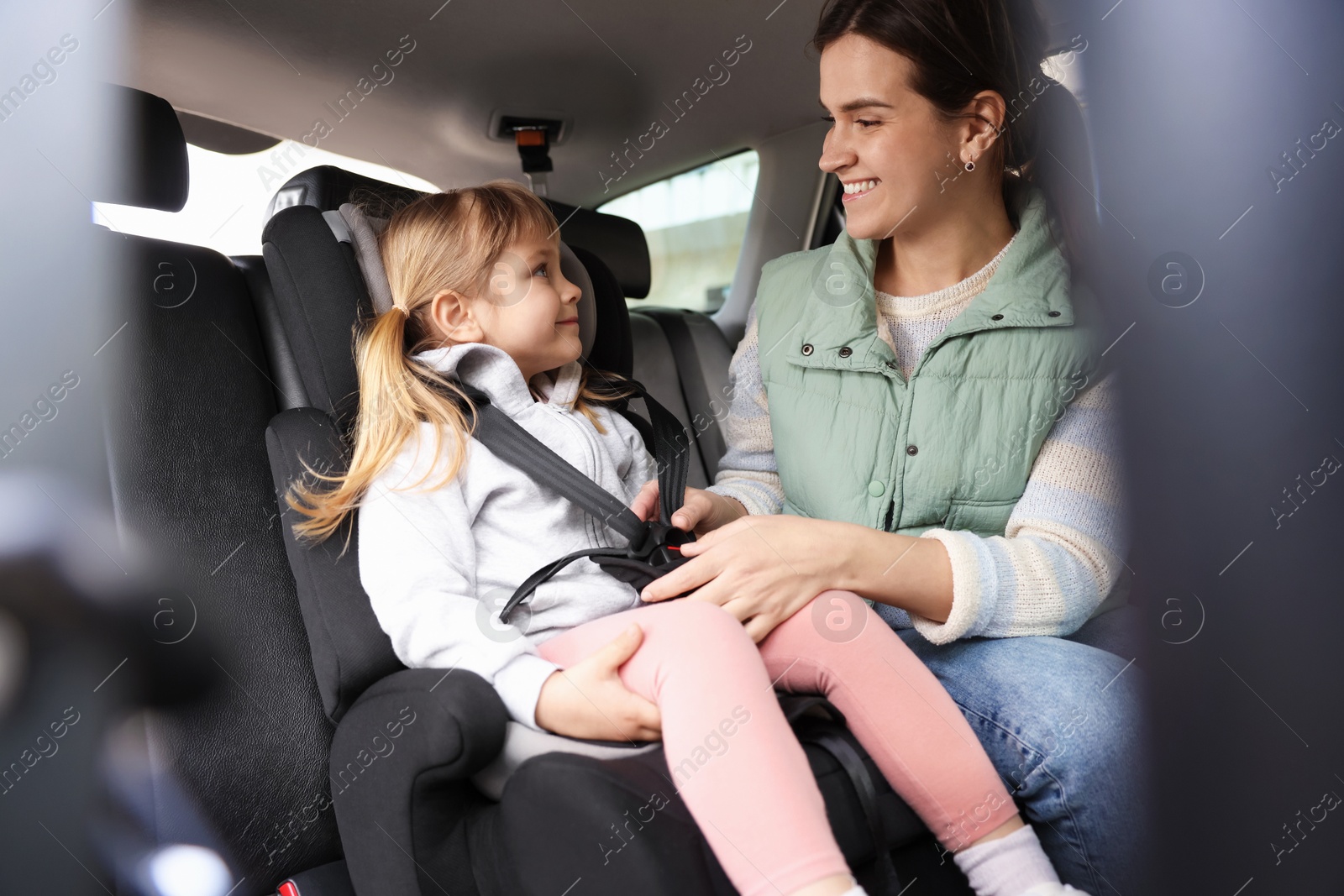 Happy mother fastening her daughter in child safety seat inside car Photo of Happy mother fastening her daughter in child safety seat inside car