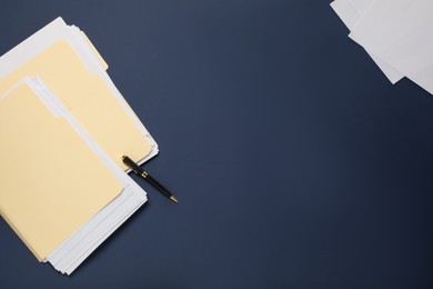 Photo of File folders with papers and pen on dark blue background, flat lay. Space for text