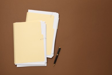 Photo of File folders with papers and pen on brown background, flat lay. Space for text