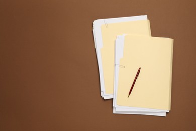 Photo of File folders with papers and pen on brown background, top view. Space for text