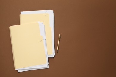 Photo of File folders with papers and pen on brown background, flat lay. Space for text