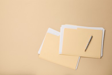 Photo of File folders with papers and pen on beige background, flat lay. Space for text