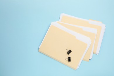 Photo of File folders with papers and binder clips on light blue background, flat lay. Space for text