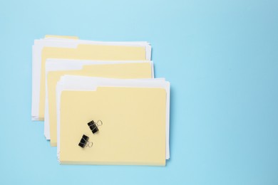 Photo of File folders with papers and binder clips on light blue background, flat lay. Space for text