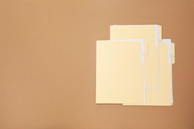 Photo of File folders with papers on light brown background, flat lay. Space for text