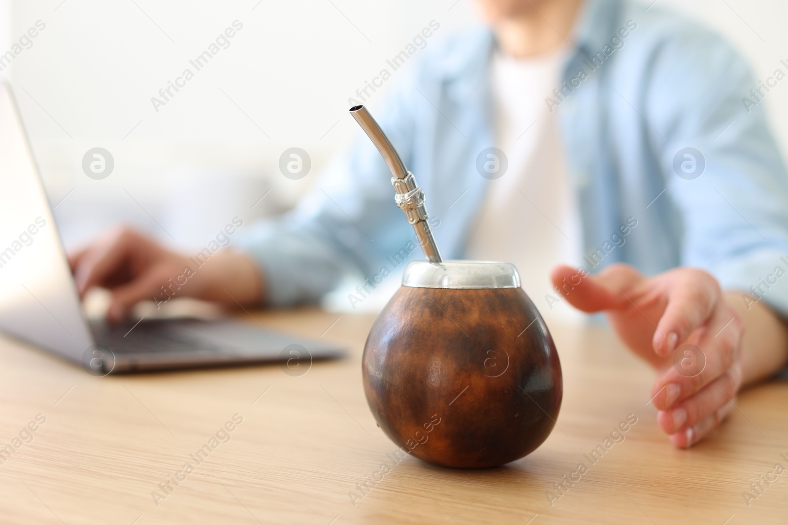 Man using laptop at wooden table indoors, focus on traditional yerba mate tea Photo of Man using laptop at wooden table indoors, focus on traditional yerba mate tea