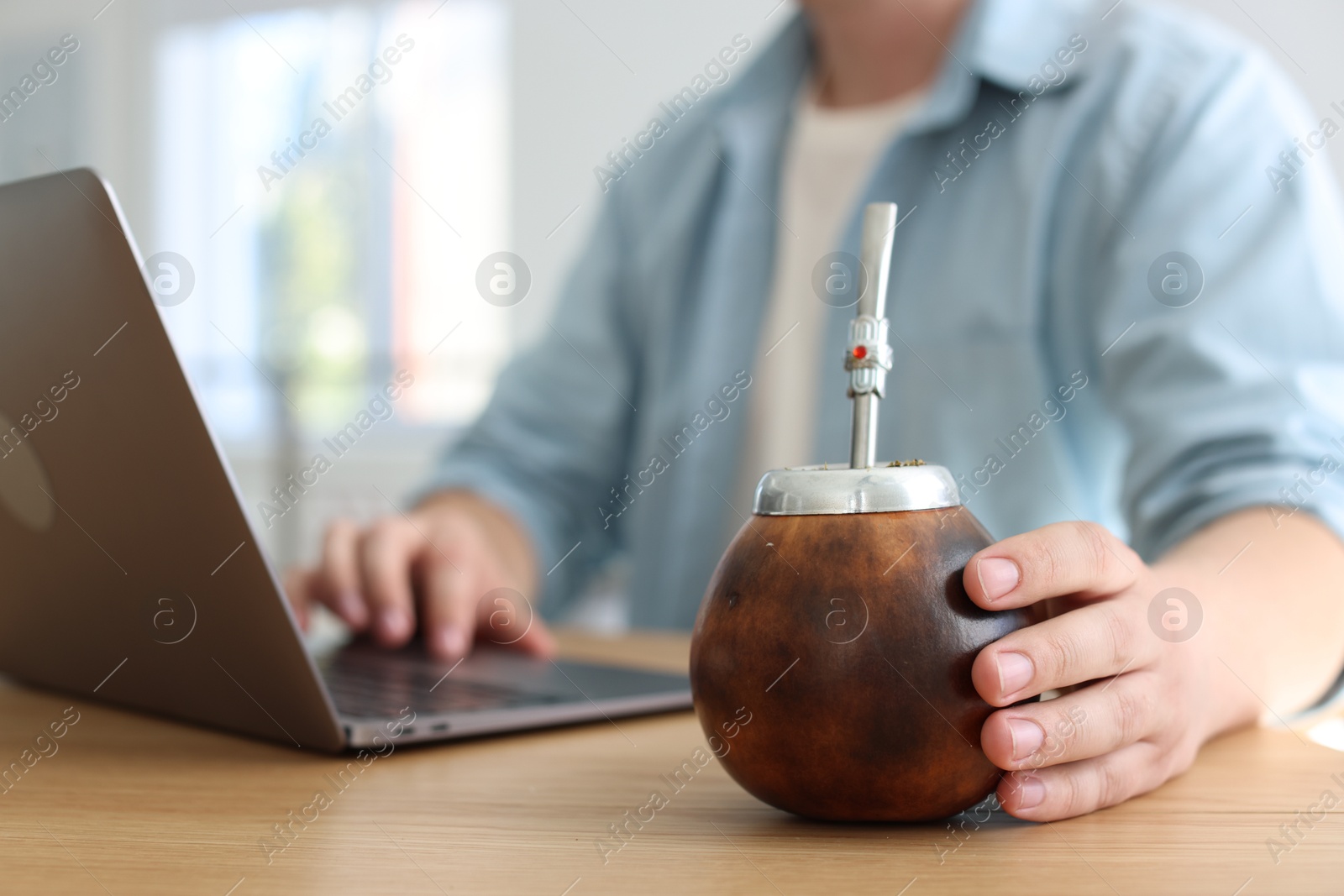 Man using laptop at wooden table indoors, focus on traditional yerba mate tea Photo of Man using laptop at wooden table indoors, focus on traditional yerba mate tea