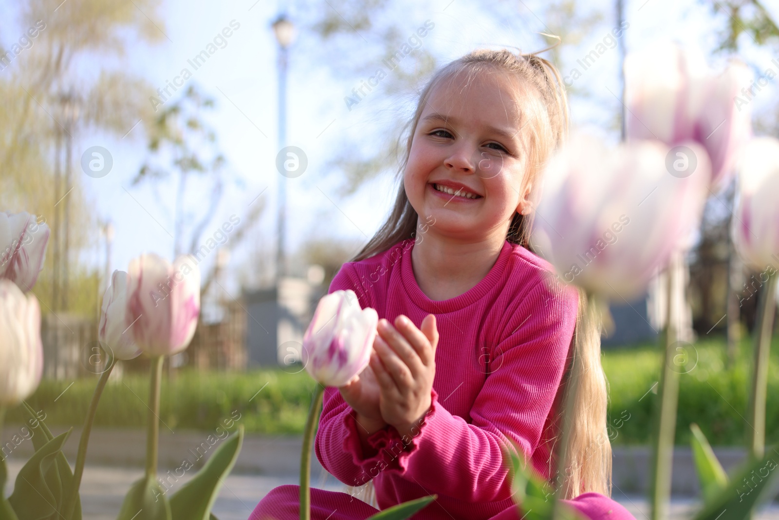 Photo of Cute little girl near beautiful pink tulips outdoors