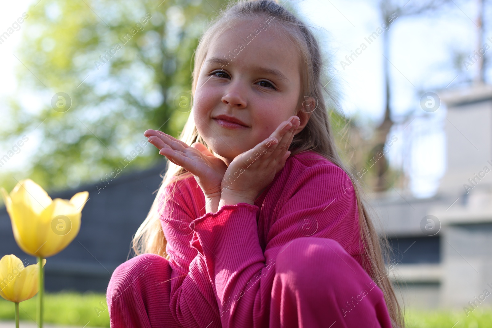 Photo of Cute little girl near beautiful yellow tulips outdoors