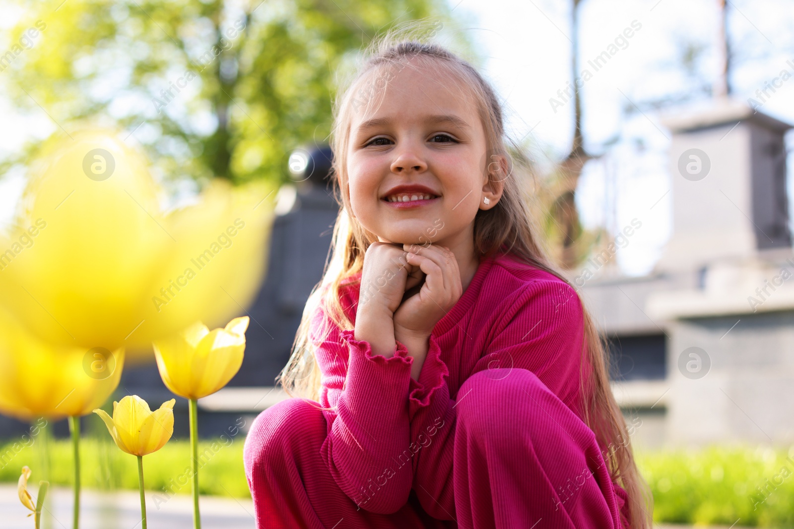 Photo of Cute little girl near beautiful yellow tulips outdoors