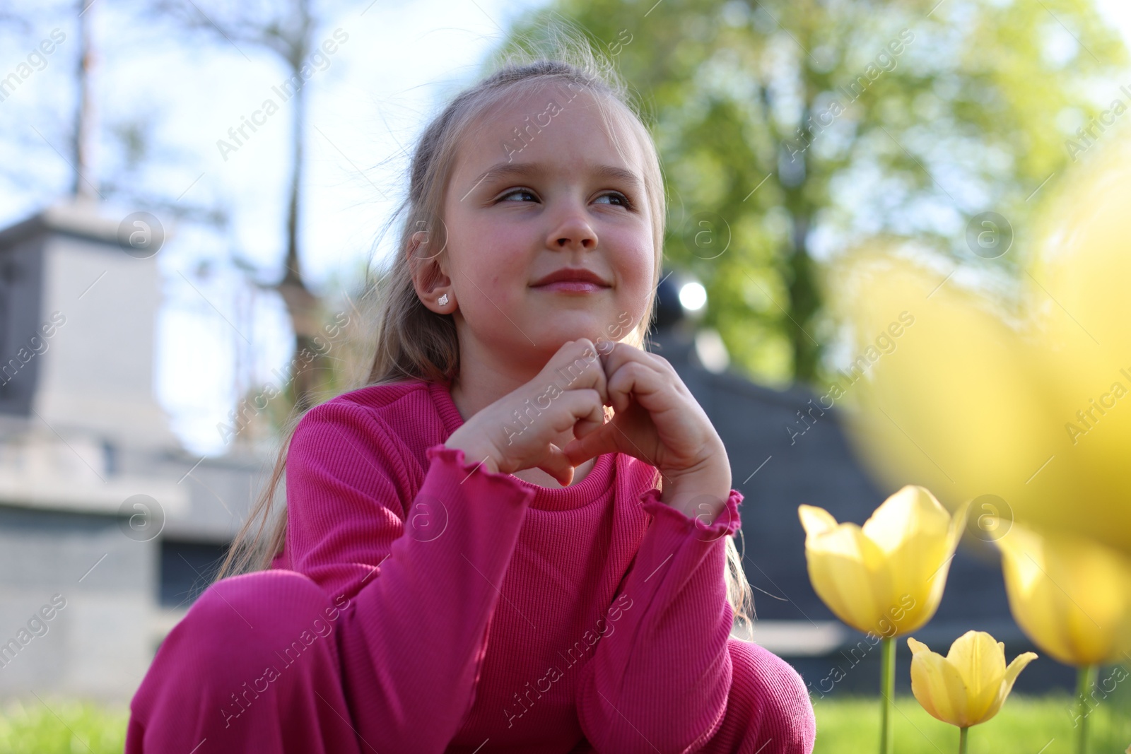Photo of Cute little girl near beautiful yellow tulips outdoors