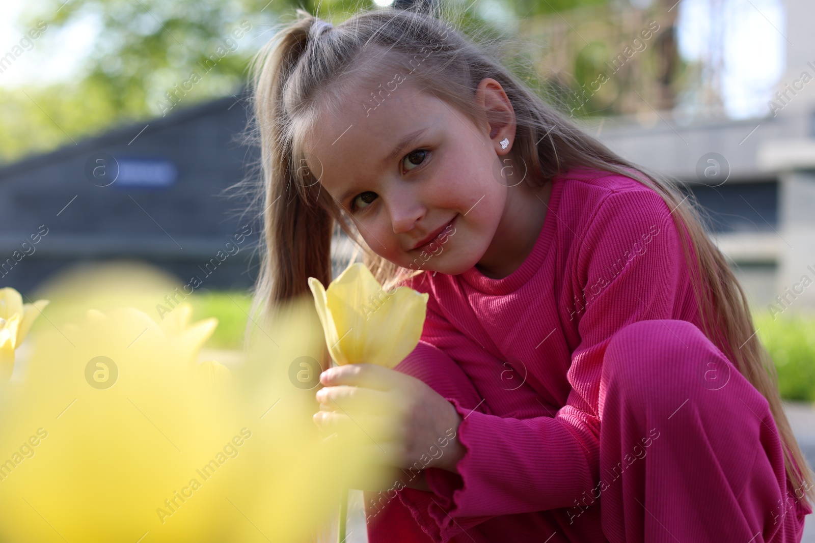 Photo of Cute little girl near beautiful yellow tulips outdoors