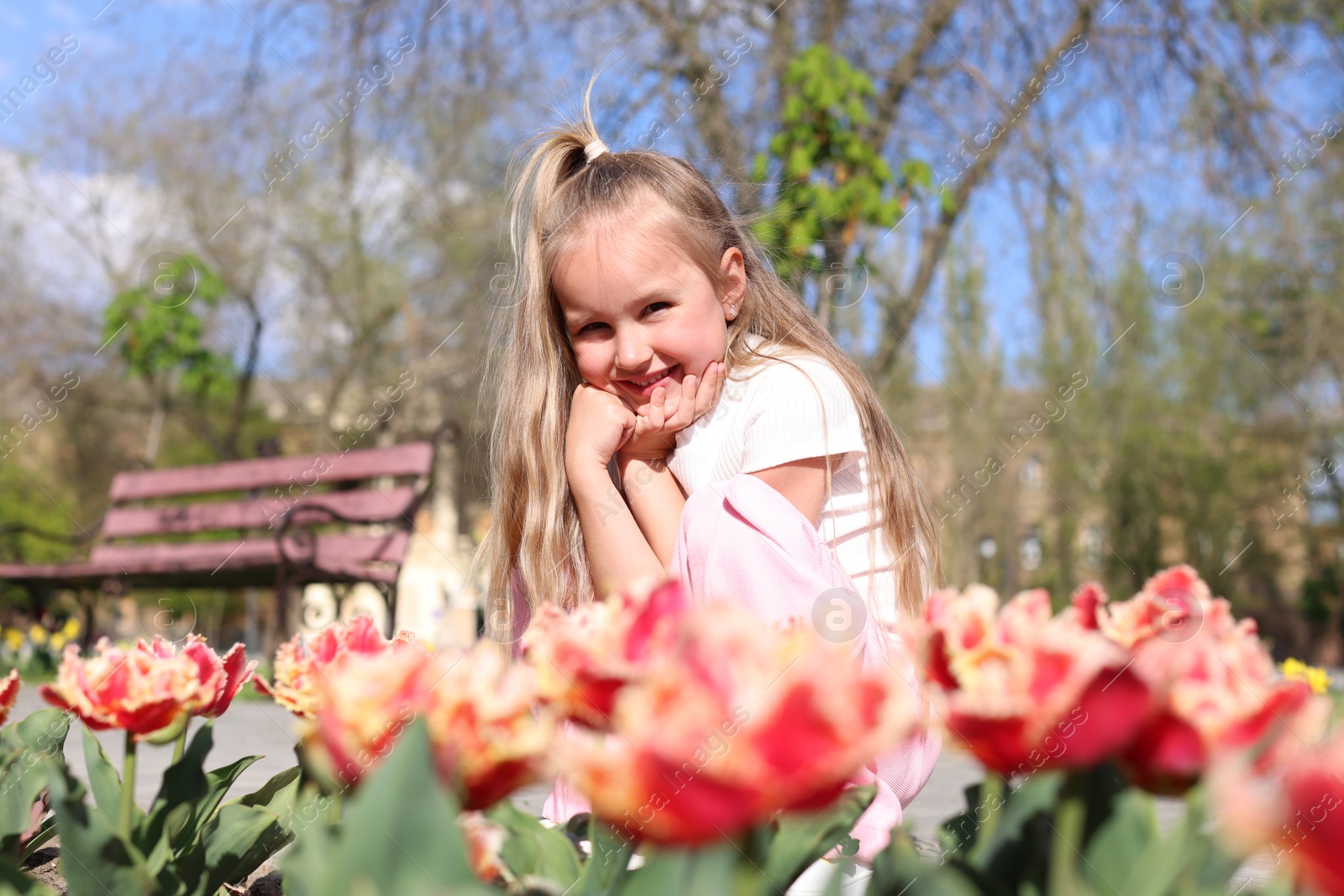 Photo of Cute little girl near beautiful tulips outdoors