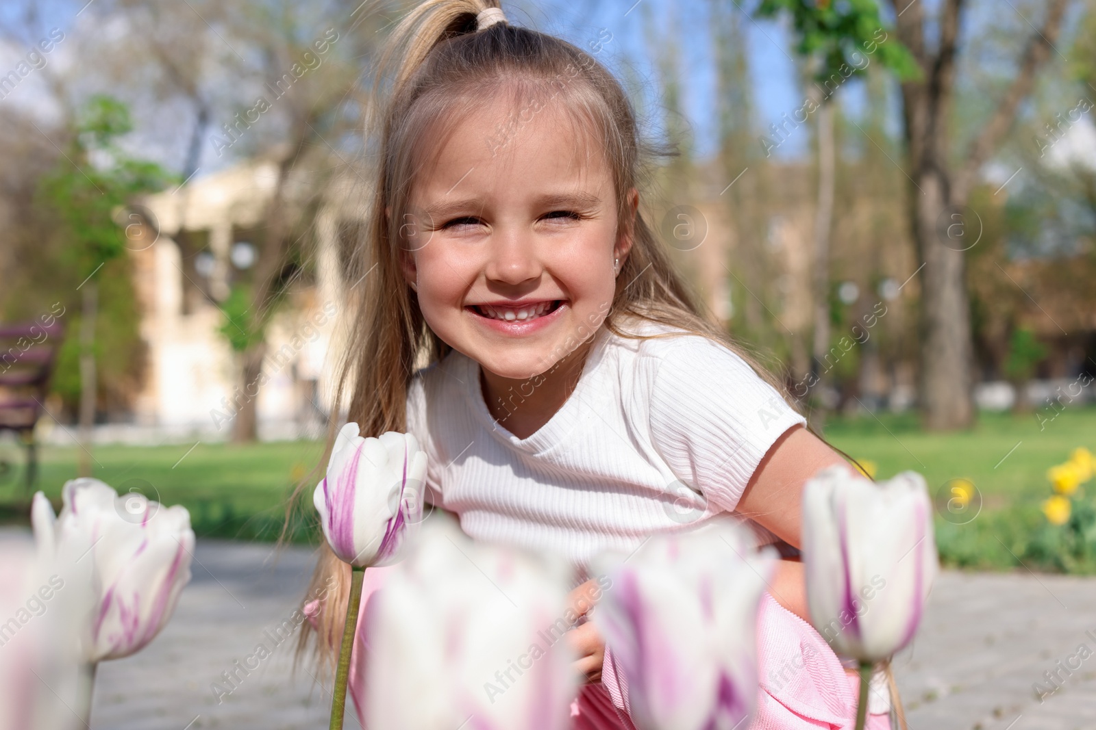 Photo of Cute little girl near beautiful tulips outdoors