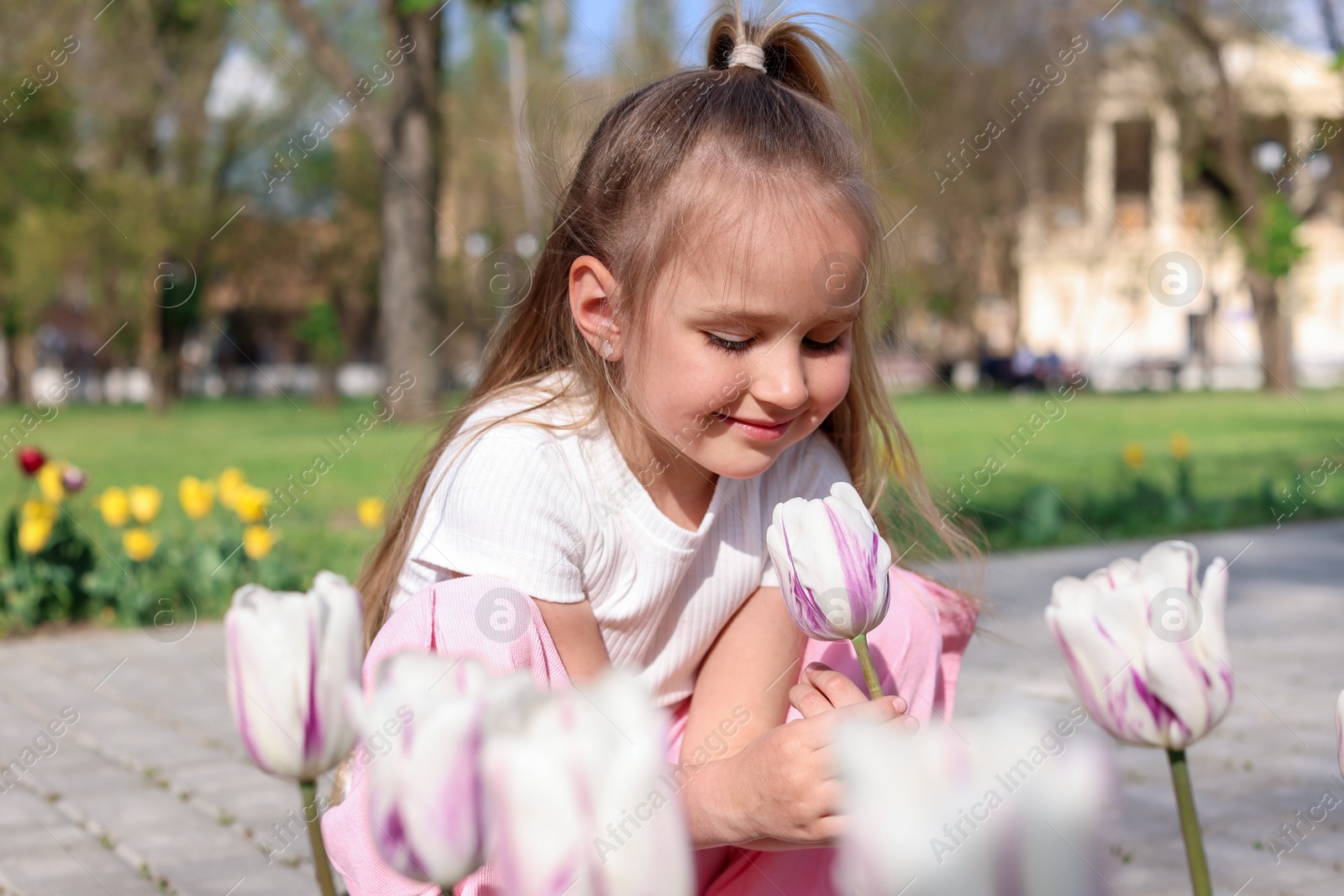 Photo of Cute little girl near beautiful tulips outdoors