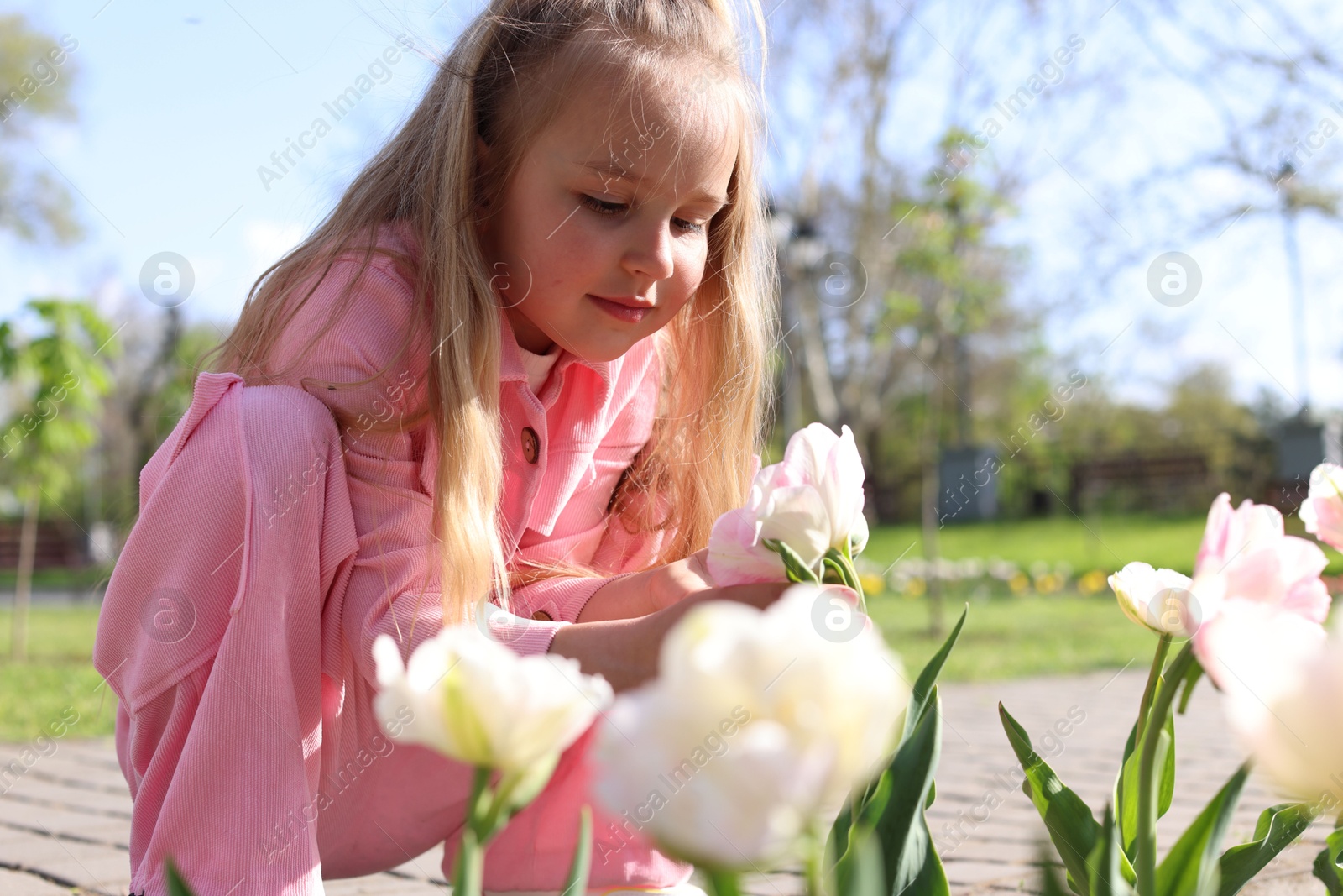 Photo of Cute little girl near beautiful tulips outdoors