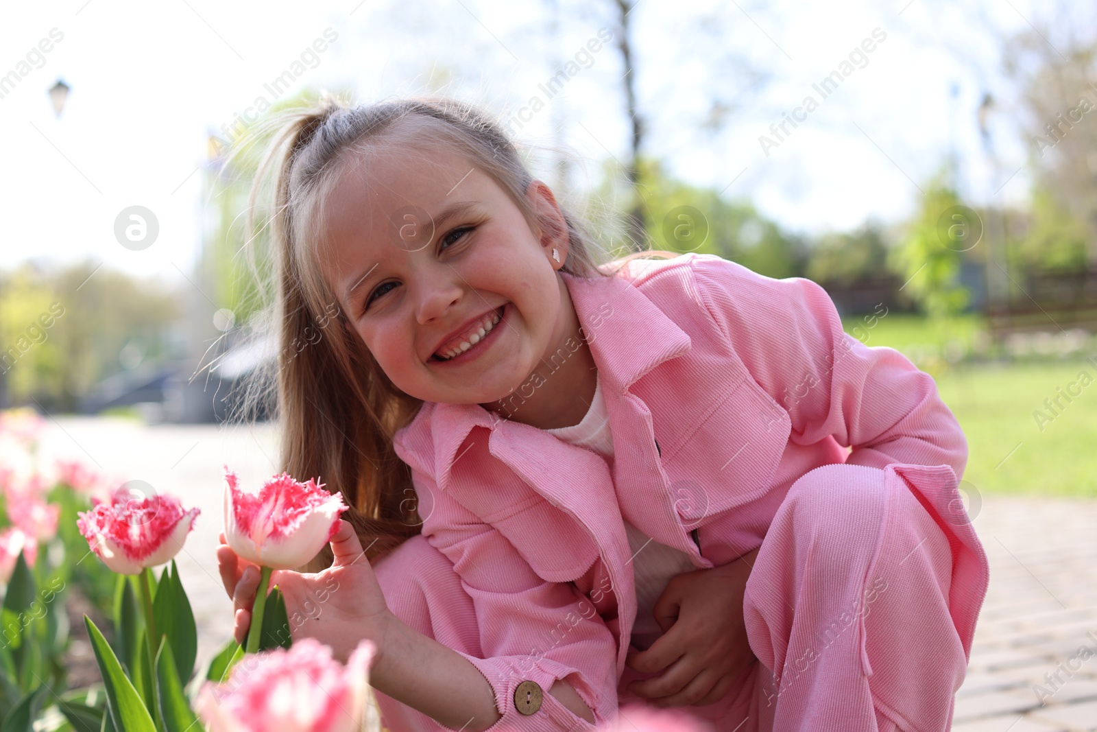 Cute little girl near beautiful pink tulips outdoors Photo of Cute little girl near beautiful pink tulips outdoors