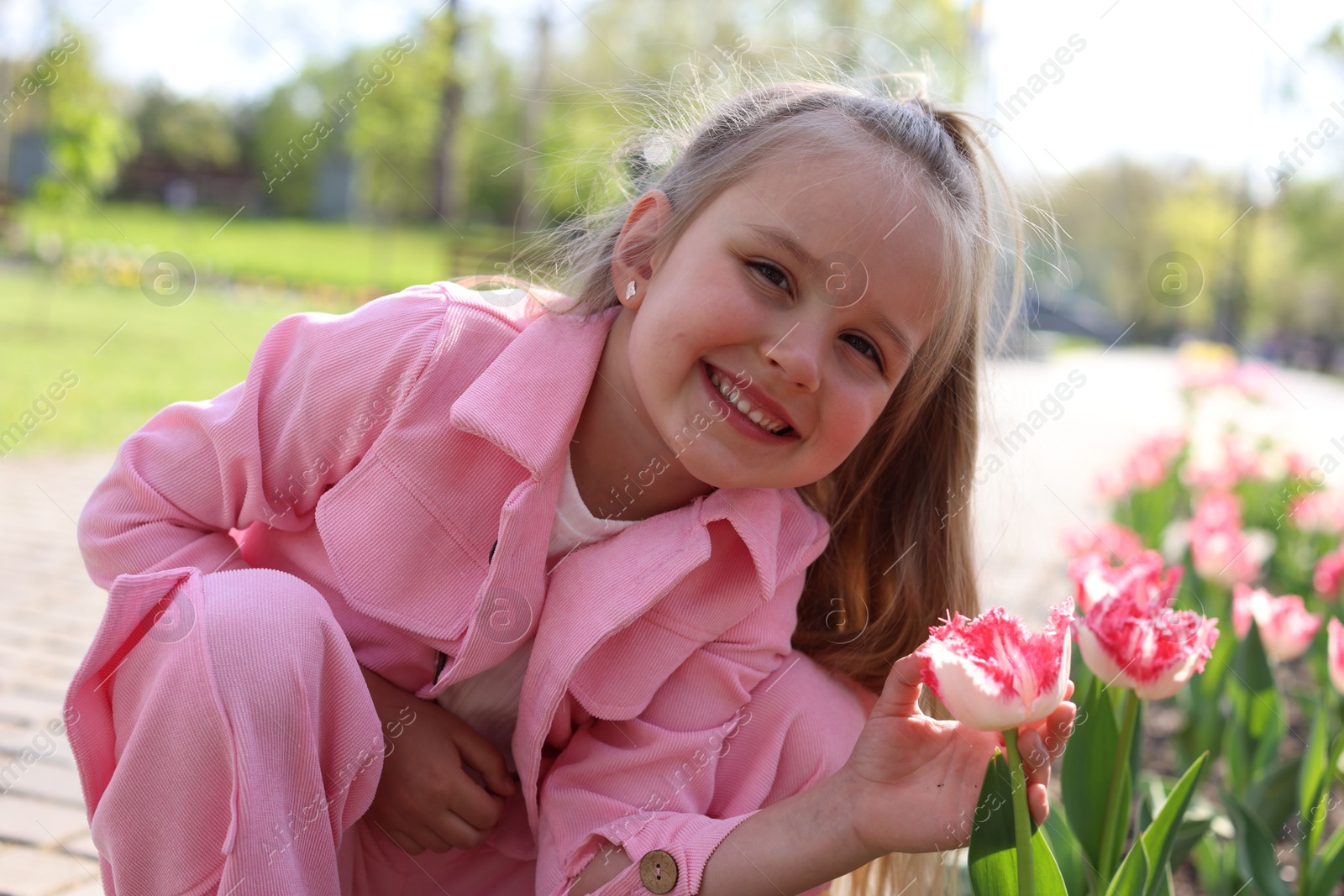 Photo of Cute little girl near beautiful pink tulips outdoors