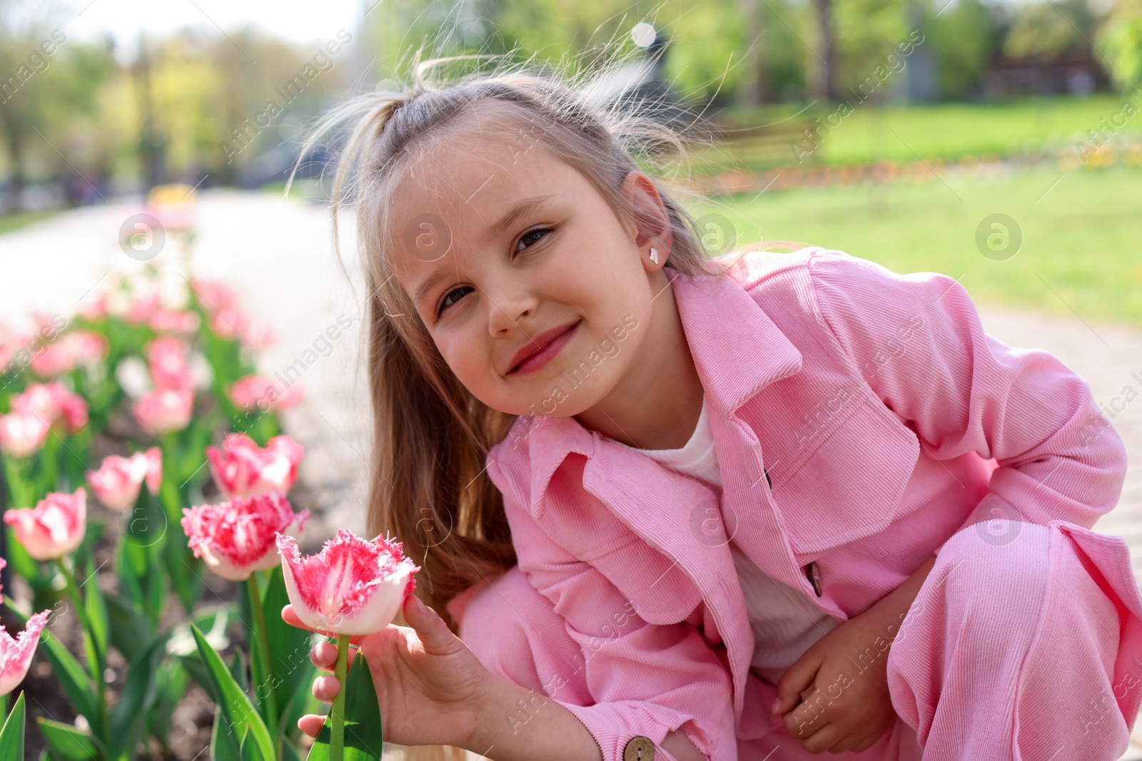 Photo of Cute little girl near beautiful pink tulips outdoors