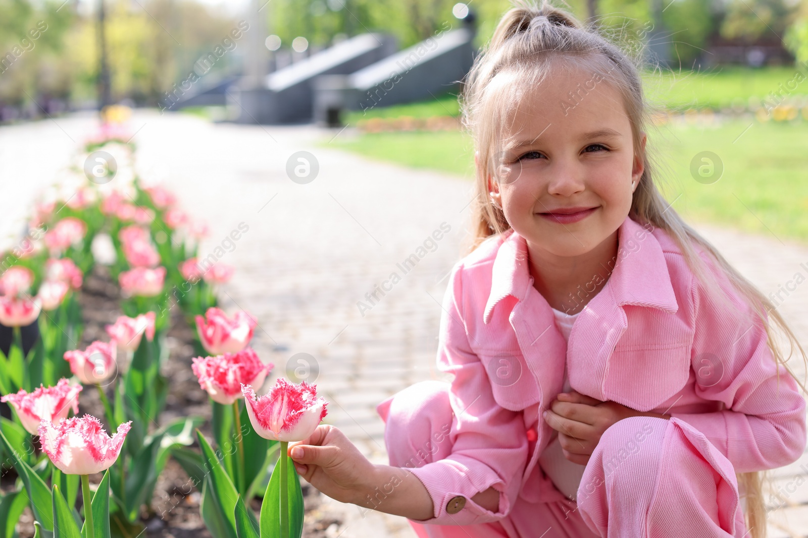 Photo of Cute little girl near beautiful pink tulips outdoors