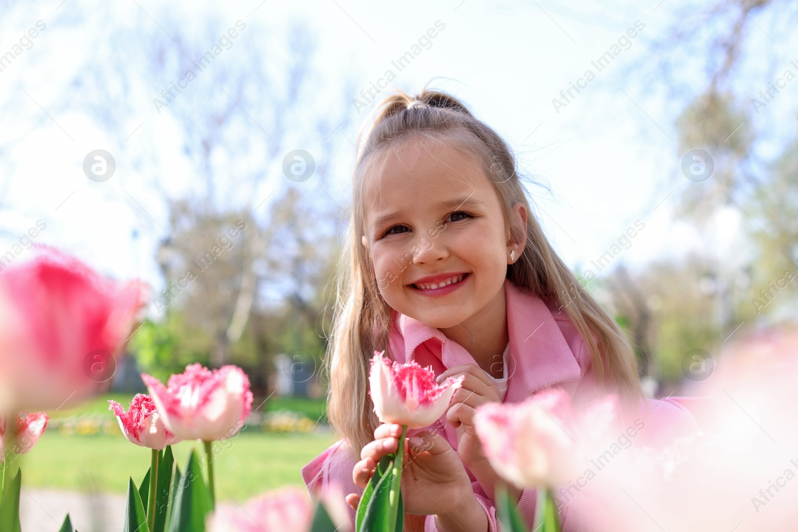 Photo of Cute little girl near beautiful pink tulips outdoors