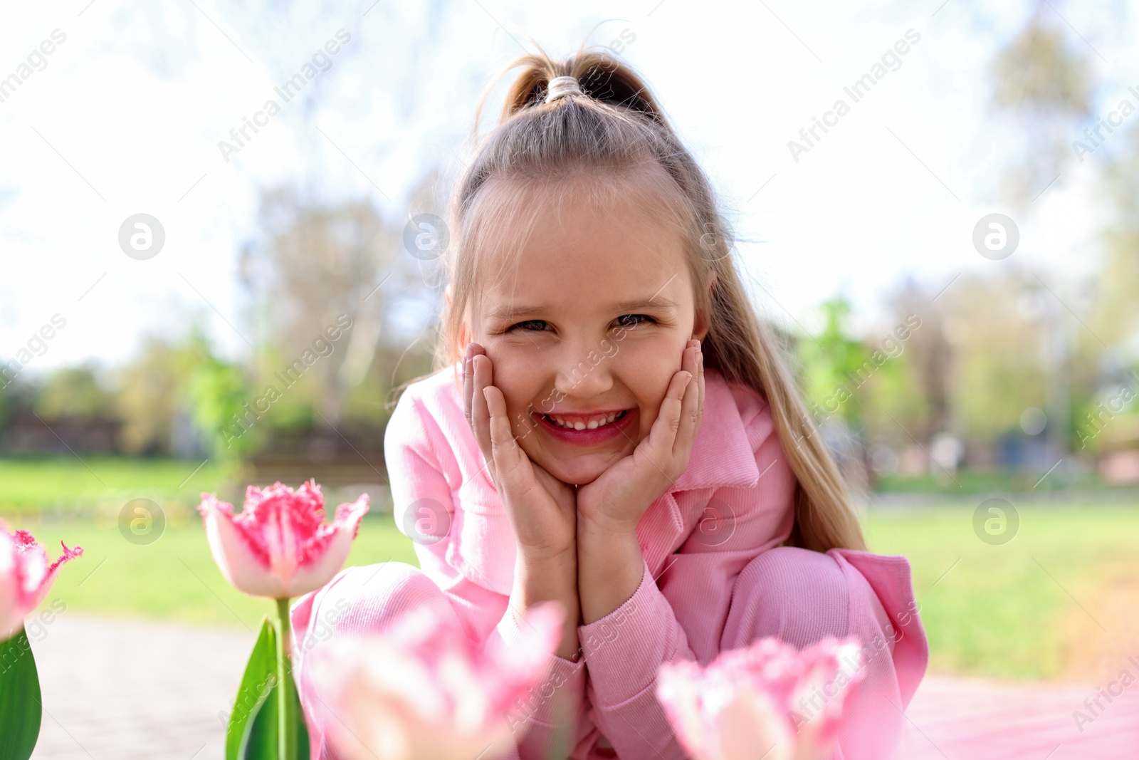 Cute little girl near beautiful pink tulips outdoors Photo of Cute little girl near beautiful pink tulips outdoors