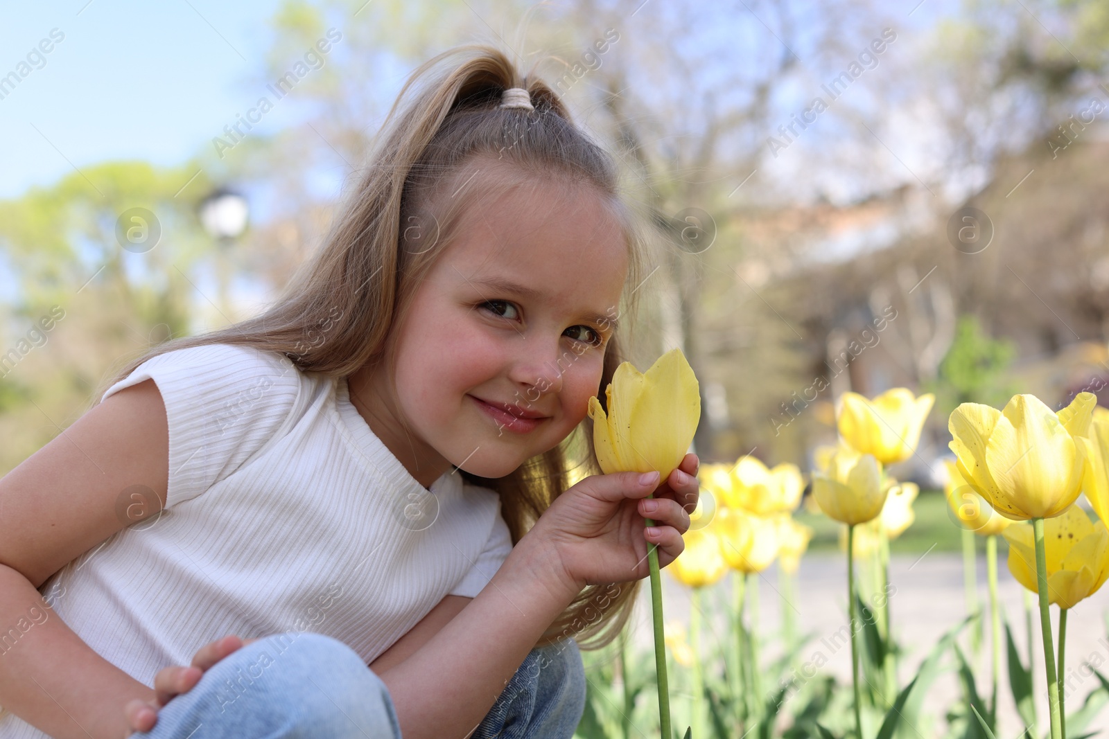 Photo of Cute little girl near beautiful yellow tulips outdoors