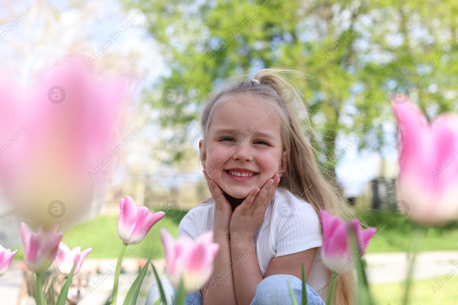 Cute little girl near beautiful pink tulips outdoors Photo of Cute little girl near beautiful pink tulips outdoors