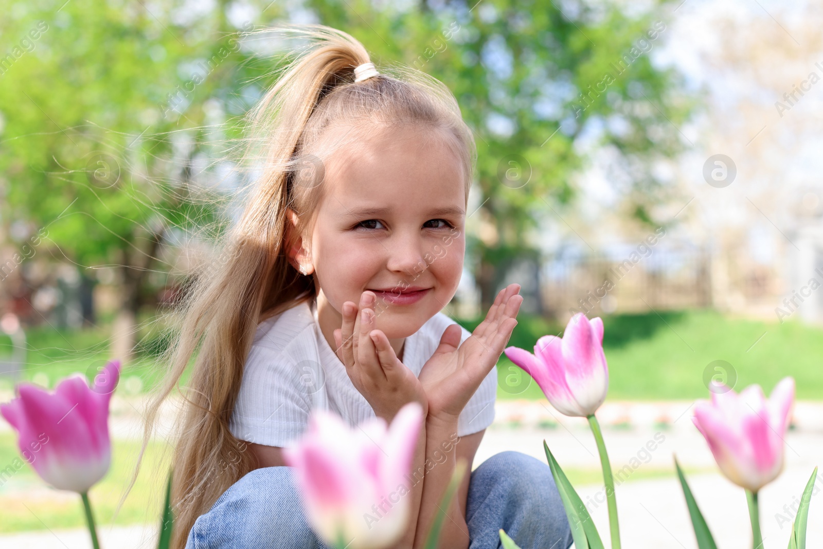 Photo of Cute little girl near beautiful pink tulips outdoors