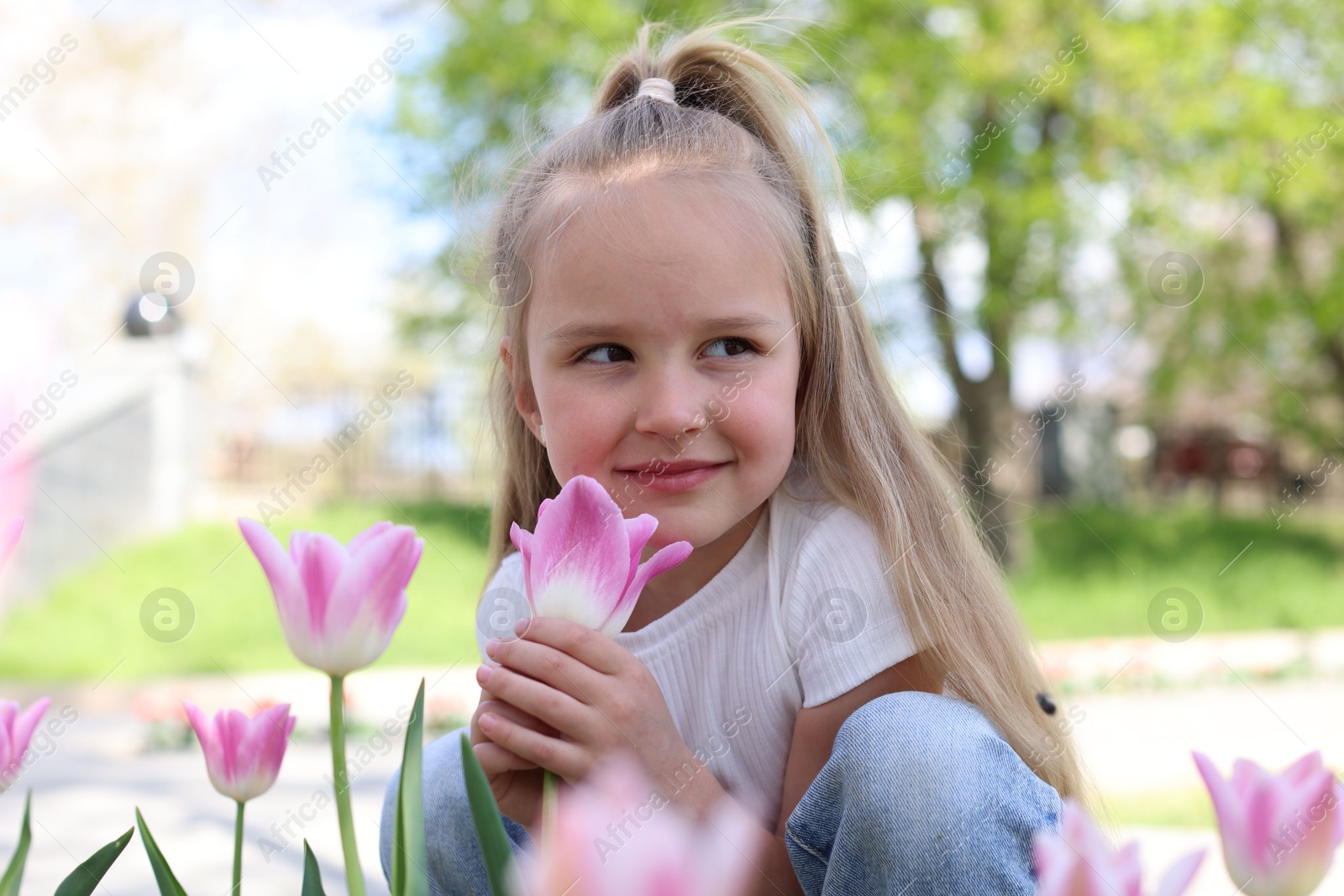 Photo of Cute little girl near beautiful pink tulips outdoors