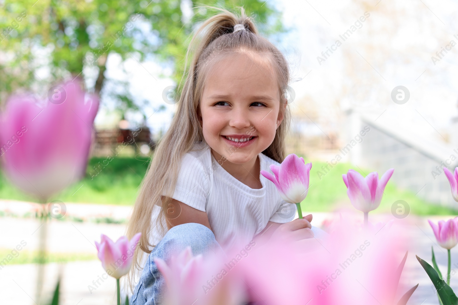 Cute little girl near beautiful pink tulips outdoors Photo of Cute little girl near beautiful pink tulips outdoors