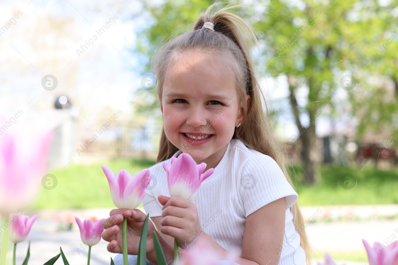 Photo of Cute little girl near beautiful pink tulips outdoors