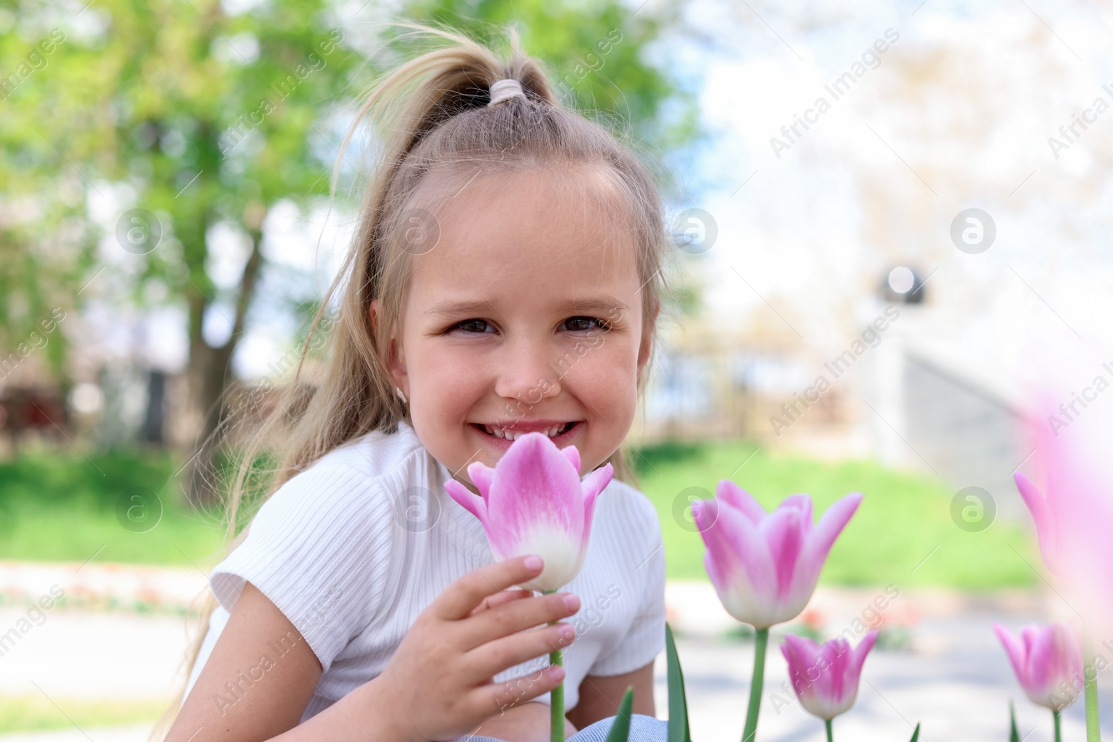 Photo of Cute little girl near beautiful pink tulips outdoors