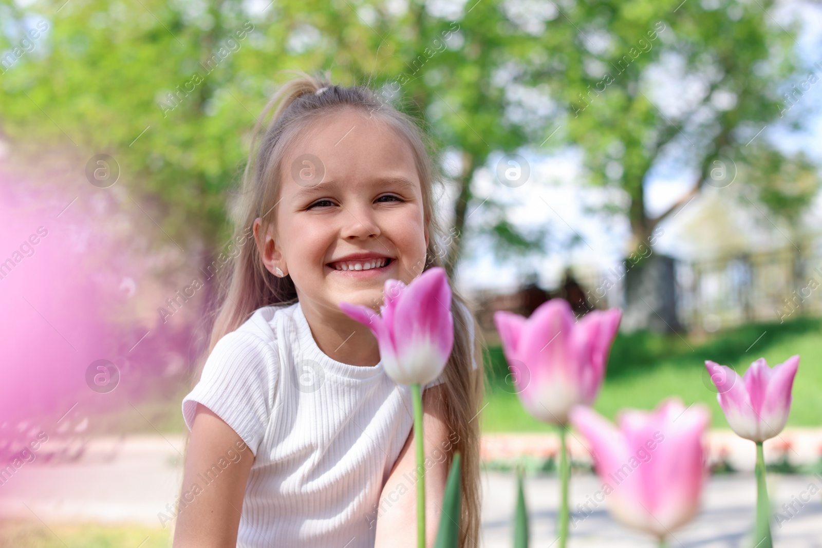 Photo of Cute little girl near beautiful pink tulips outdoors