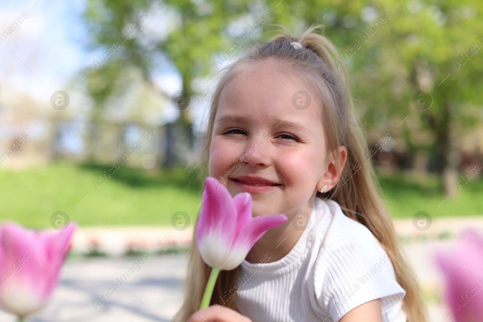 Photo of Cute little girl near beautiful pink tulips outdoors