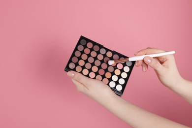 Photo of Woman with eyeshadow palette and brush on pink background, closeup