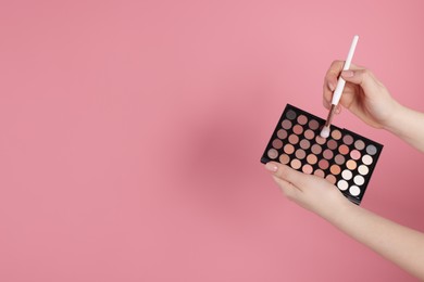 Photo of Woman with eyeshadow palette and brush on pink background, closeup. Space for text