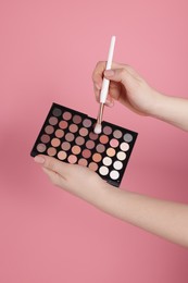 Photo of Woman with eyeshadow palette and brush on pink background, closeup