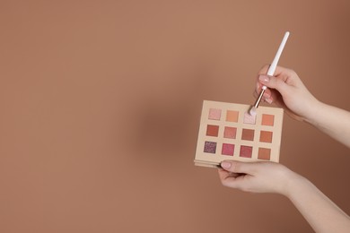 Photo of Woman with eyeshadow palette and brush on beige background, closeup. Space for text