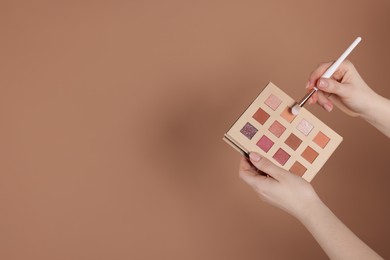 Photo of Woman with eyeshadow palette and brush on beige background, closeup. Space for text