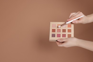 Photo of Woman with eyeshadow palette and brush on beige background, closeup. Space for text