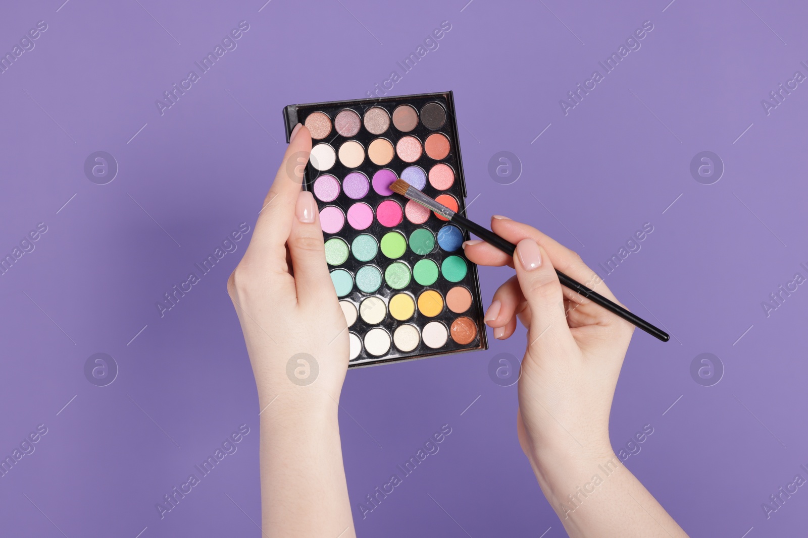 Woman with eyeshadow palette and brush on violet background, closeup Photo of Woman with eyeshadow palette and brush on violet background, closeup
