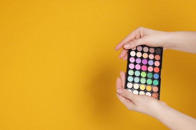 Photo of Woman with bright eyeshadow palette on yellow background, closeup. Space for text