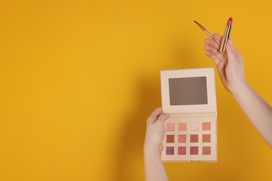 Photo of Woman with eyeshadow palette, lipstick and brush on yellow background, closeup. Space for text